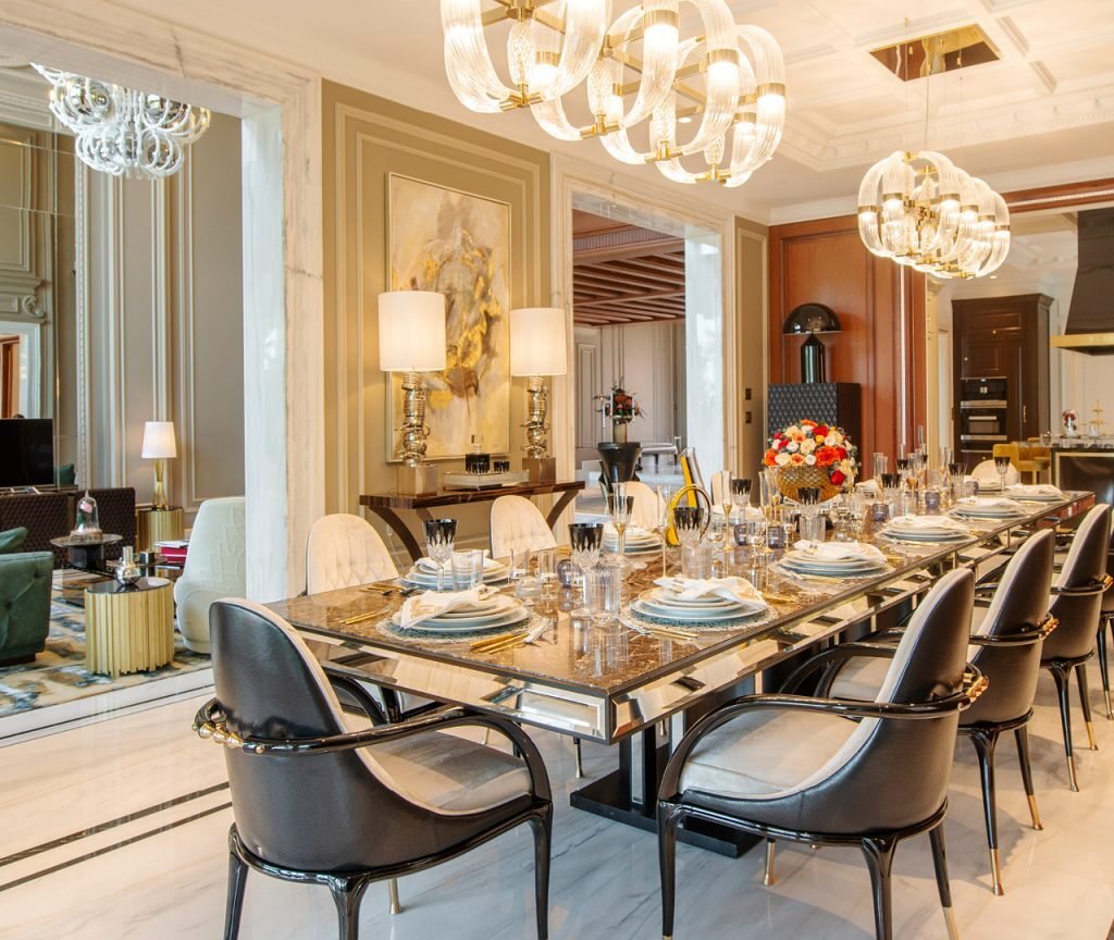 Villa dining room fit out in Dubai featuring a formal dining table, decorative wall panels and statement chandeliers